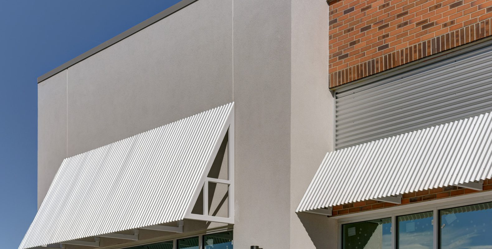 Ulster commercial building facade detail – corrugated metal sunshades and mixed brick and stucco exterior by GEM Studio Architecture
